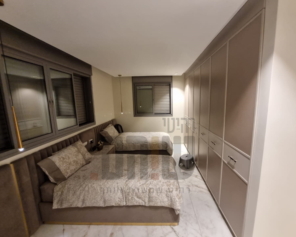 חדר שינה מעוצב עם מיטה זוגית מרופדת וארונות קיר בהתאמה אישית בגוונים חמים