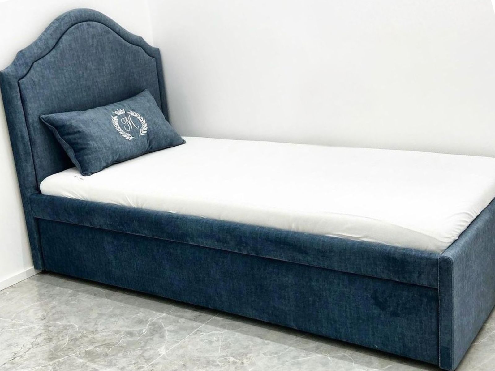 מיטת נוער מרופדת בגוון כחול, עם ראש מיטה בקווים מעוגלים ובסיס מרופד בקו ישר.