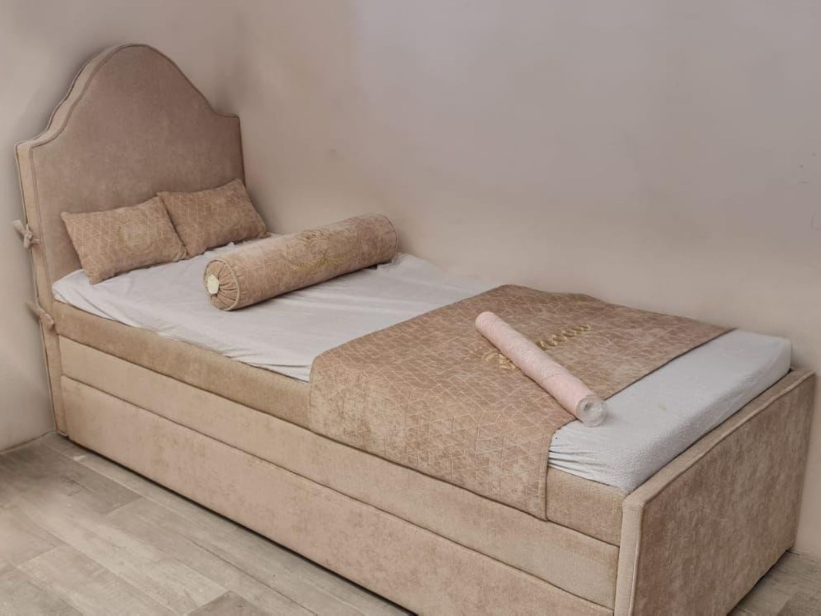 מיטת נוער מרופדת בגוון בהיר, עם ראש מיטה מעוצב בקו מעוגל ובסיס מרופד בקווים ישרים.