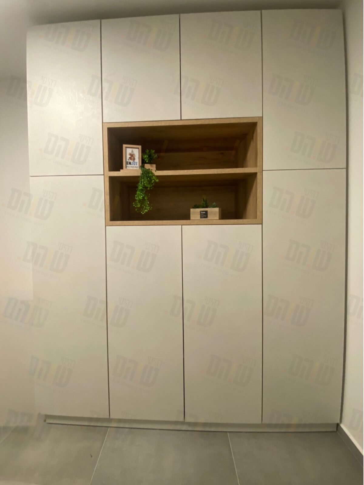 ארון קיר בעל חזית בהירה עם חלוקה אופקית, משולב נישה מרכזית כפולה בגימור עץ.
