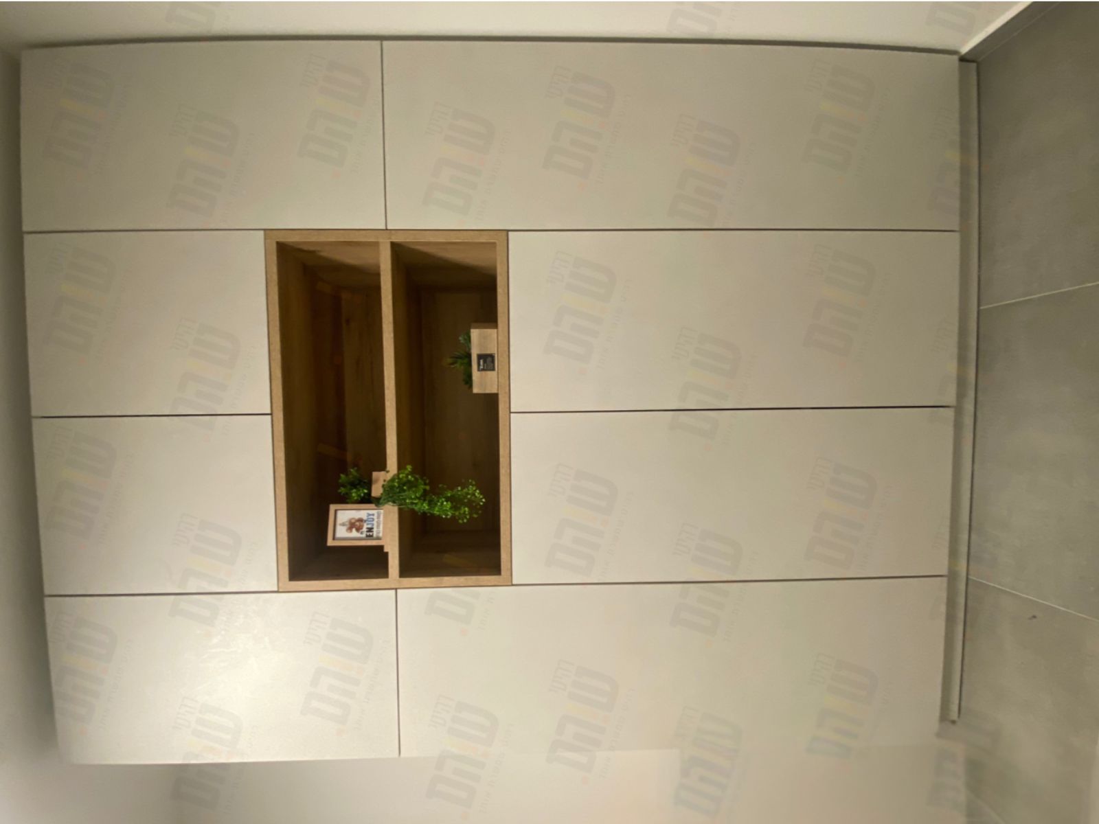 ארון קיר בעל חזית בהירה עם חלוקה אופקית, משולב נישה מרכזית כפולה בגימור עץ.