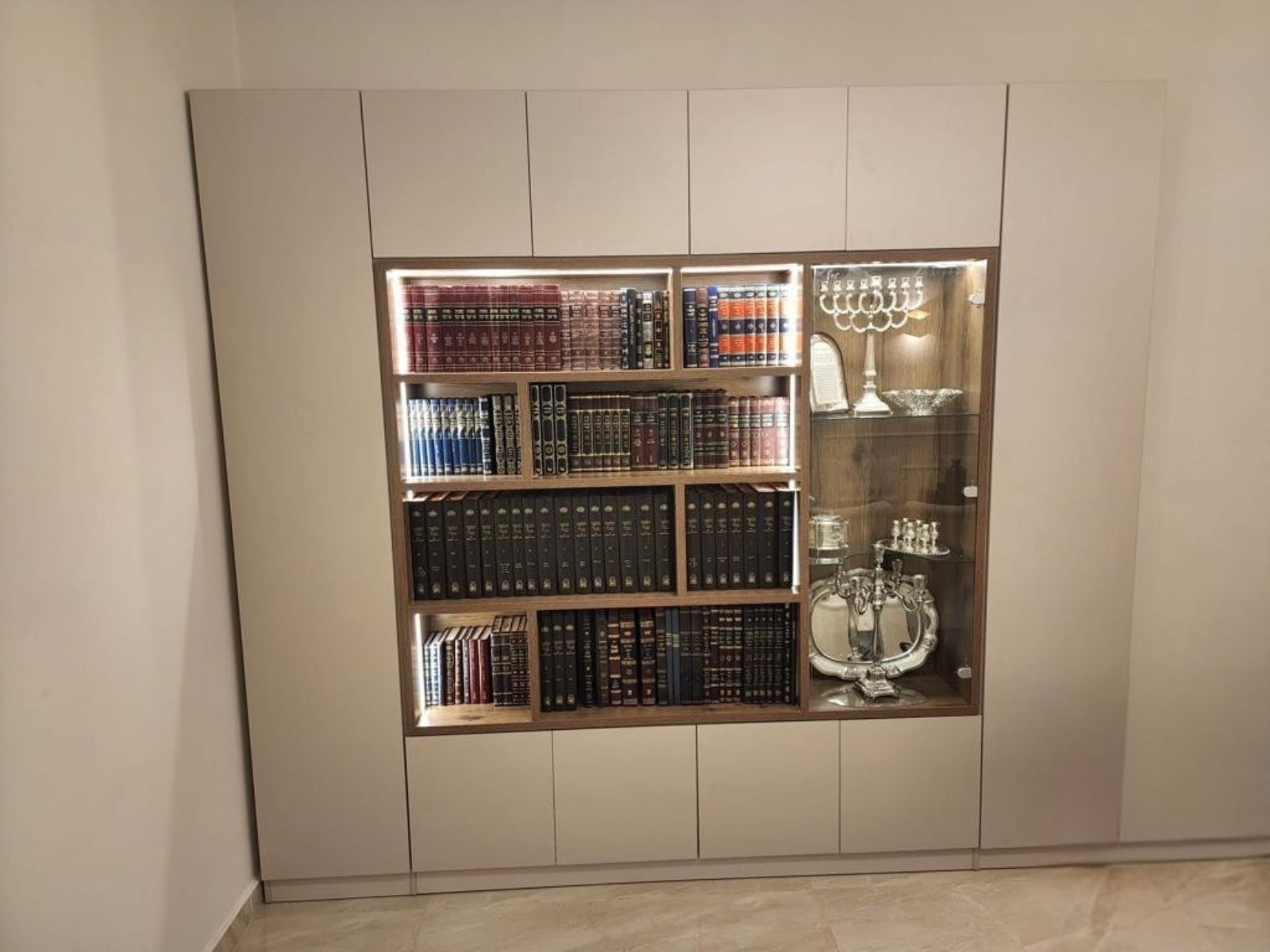 ספריית קודש מעץ מעוצבת עם שילוב תאורת לדים חמימה סביב מדפי העץ לאחסון ספרים במסגרת ארונות אחסון וכמובן וויטרינה אלגנטית