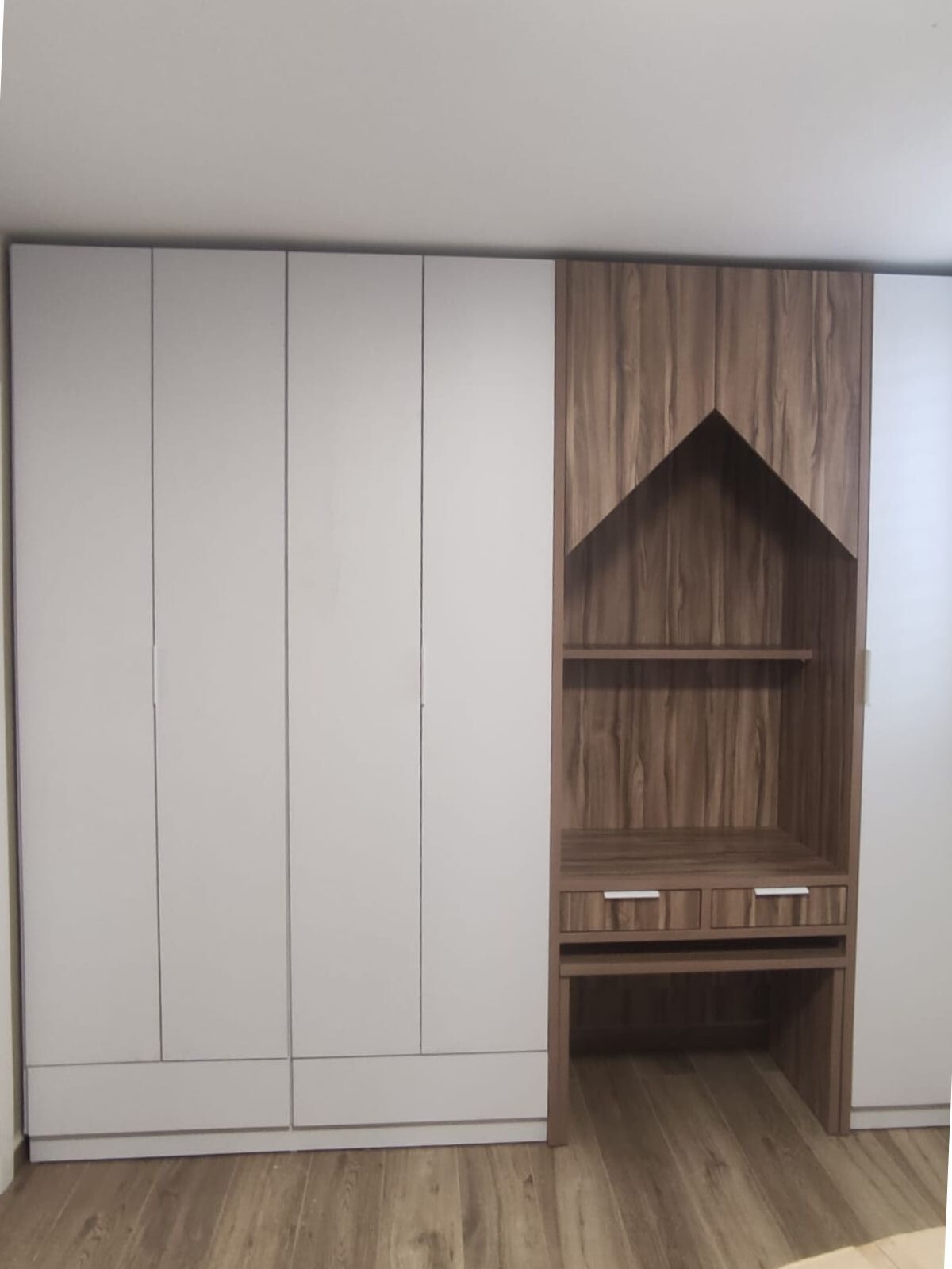 ארון בגדים עם חזית בהירה בקווים נקיים, משולב יחידת עץ צדדית עם נישה פתוחה בעיצוב גיאומטרי חדשני, שולחן כתיבה ומגירות.