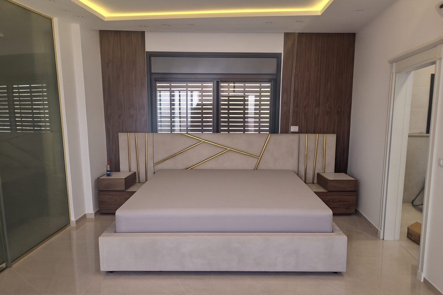 חדר שינה בעיצוב פרימיום עם מיטה מרופדת וראש מיטה גיאומטרי משולב זהב