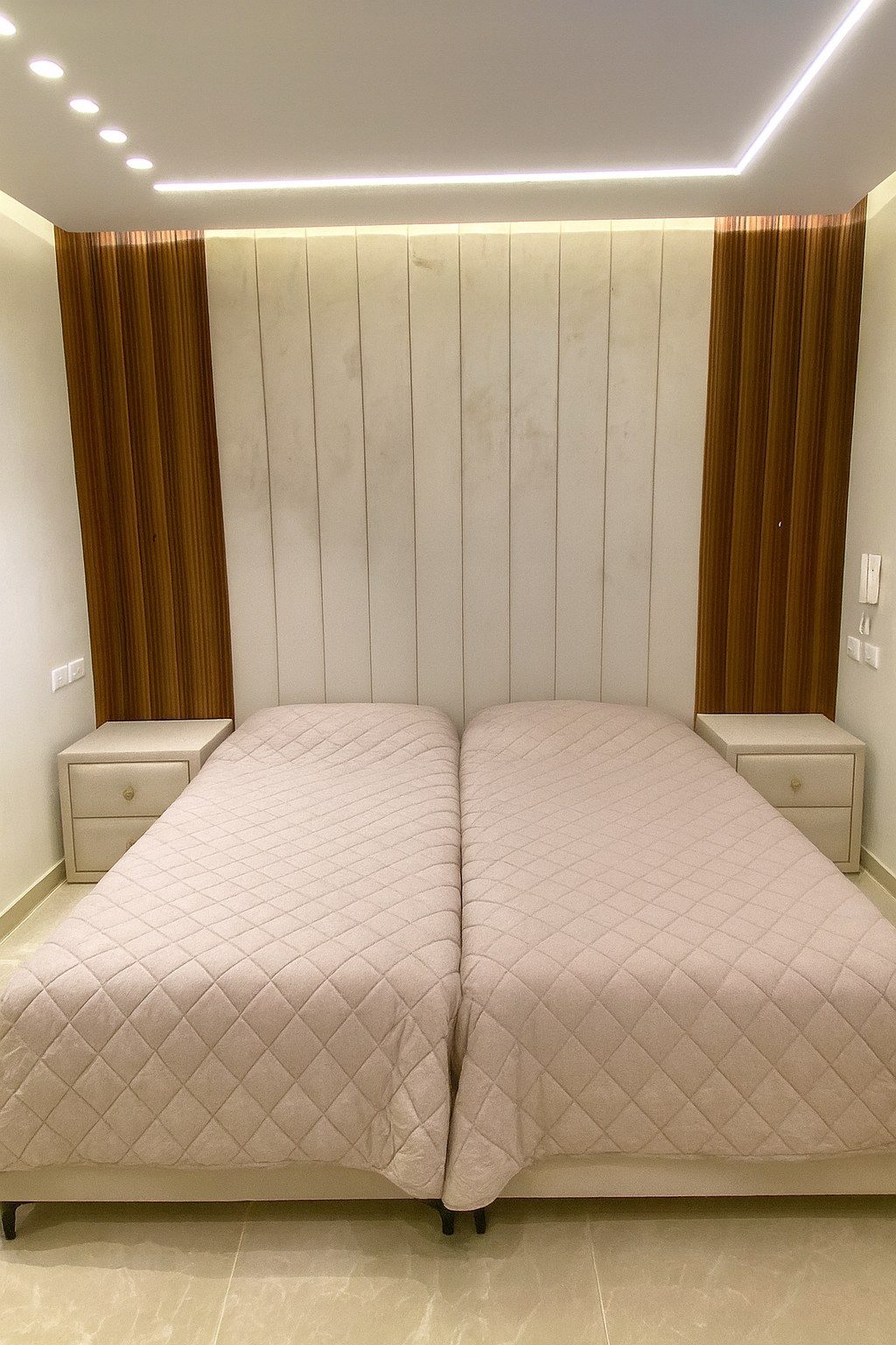 מיטות חדר שינה וראש מיטה רציף מרופד בדיגום אנכי, בשילוב חיפויי עץ ותאורה נסתרת ובהתאמה אישית לשידות דקורטיביות