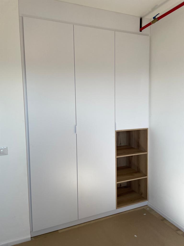 ארון קיר לבן בעיצוב נקי עם נישה פתוחה בצד בגימור עץ.