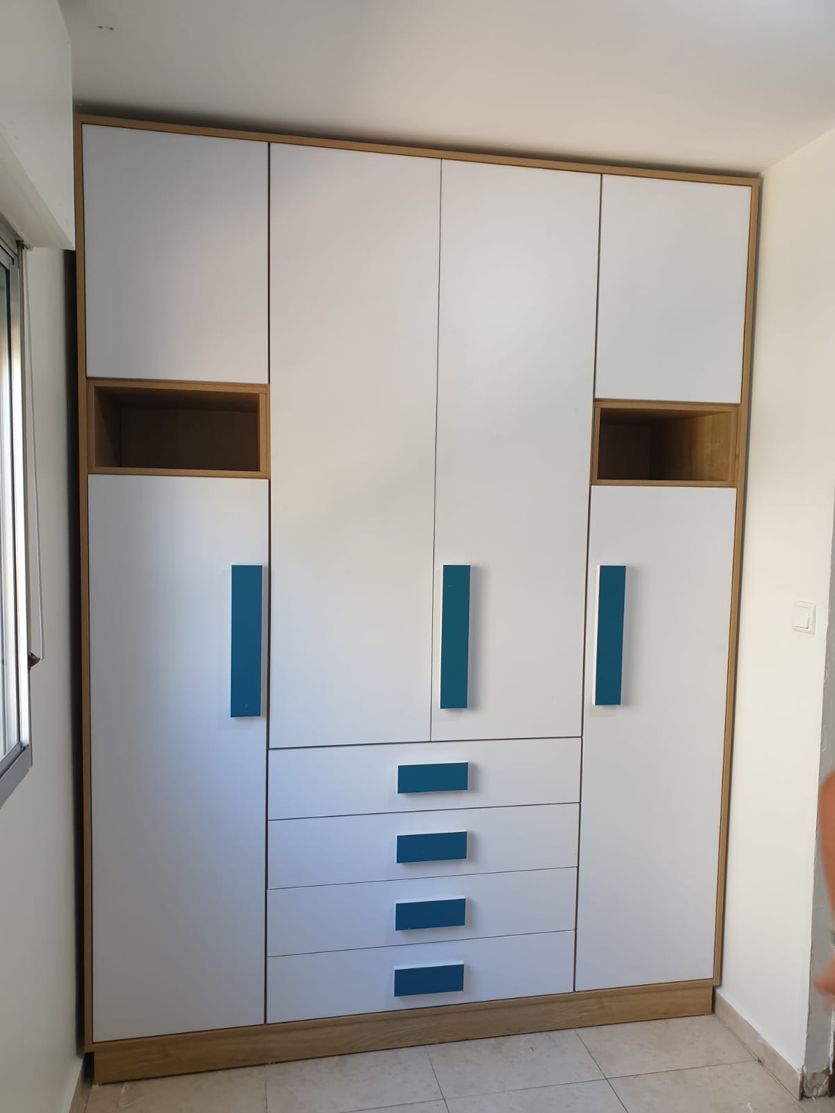 ארון פתיחה מודרני עם חזית לבנה, מסגרת עץ, ידיות כחולות בולטות ונישות פתוחות.