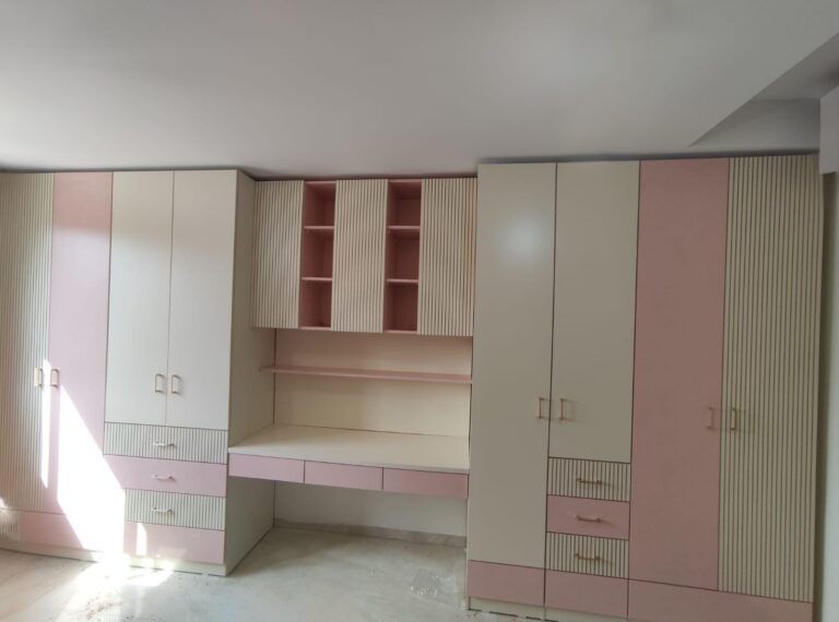 ארון בגדים בעיצוב נקי ומודרני בגוון בהיר, משולב עמדת עבודה צדדית עם משטח ומגירות בגוון ורוד רך. הארונות העליונים והנישות הפתוחות יוצרים פתרון אחסון חכם ופונקציונלי, תוך שמירה על מראה צעיר, מסודר ונעים לעין.