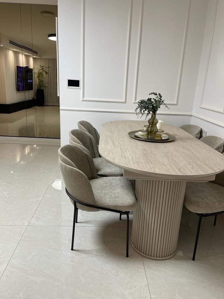 שולחן אוכל אובלי מעץ בהיר ועדין ורגליים בצורה גלילית מחורצת, בשילוב כיסאות מרופדים מעוצבים בגוון ניטרלי.