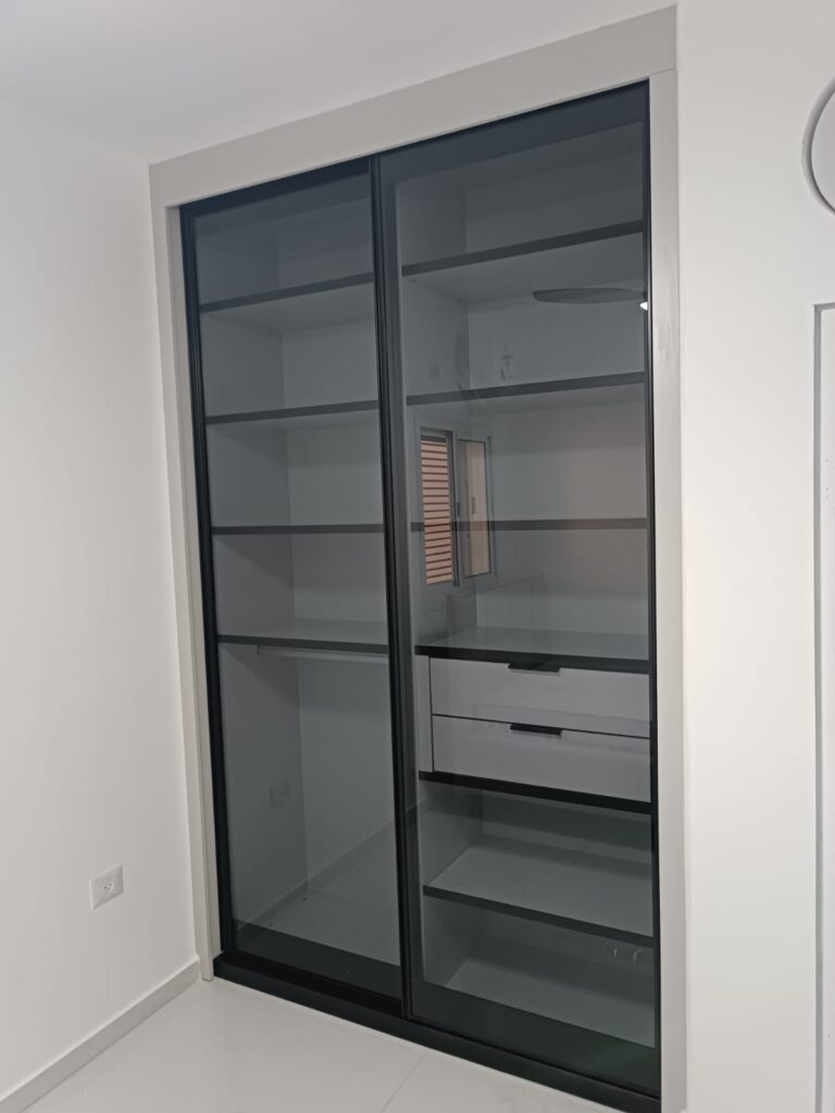 ארון הזזה עם דלתות זכוכית כהות שקופות ופנים מחולק למדפים ומגירות.
