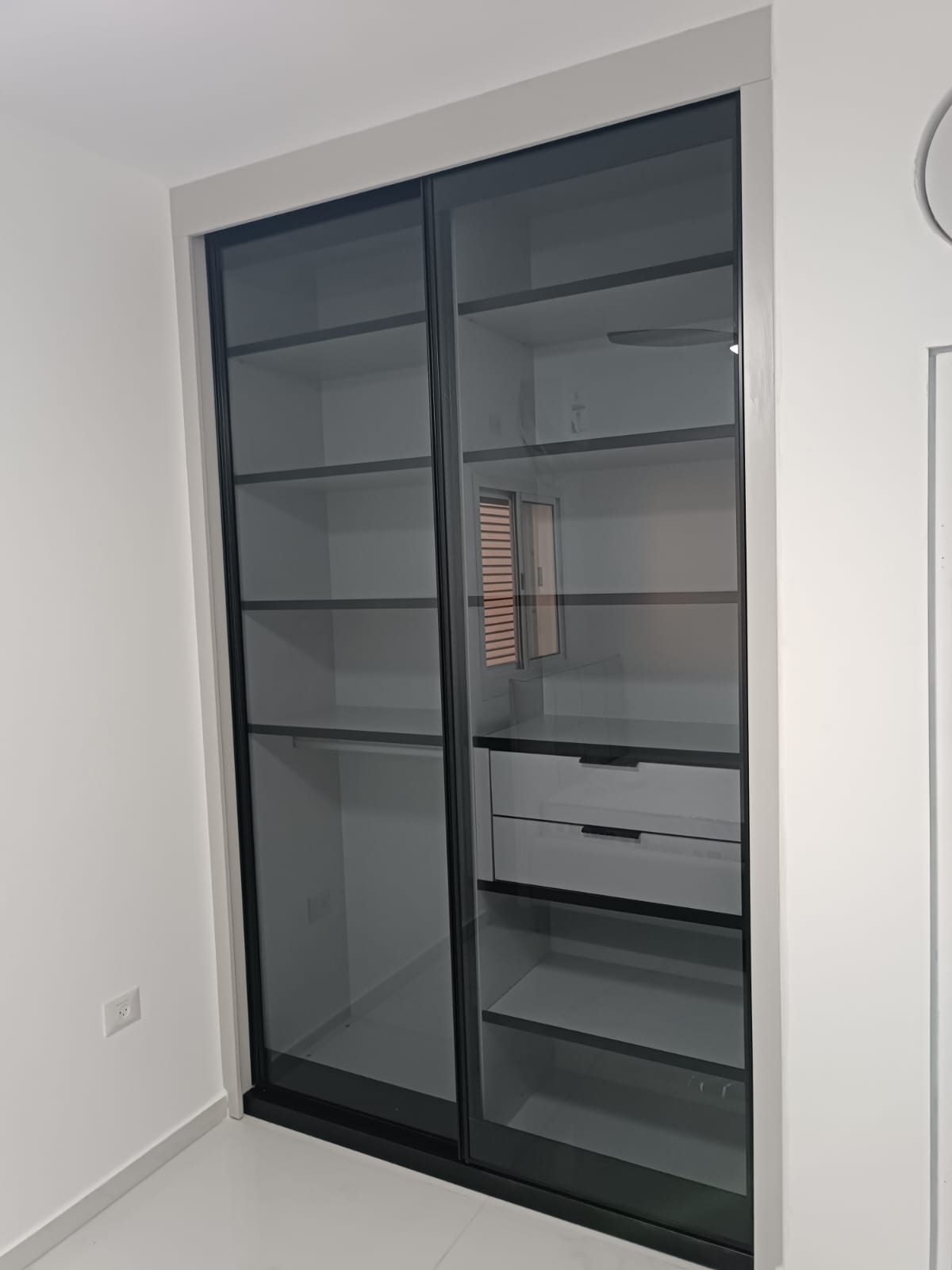 ארון הזזה עם דלתות זכוכית כהות שקופות ופנים מחולק למדפים ומגירות.