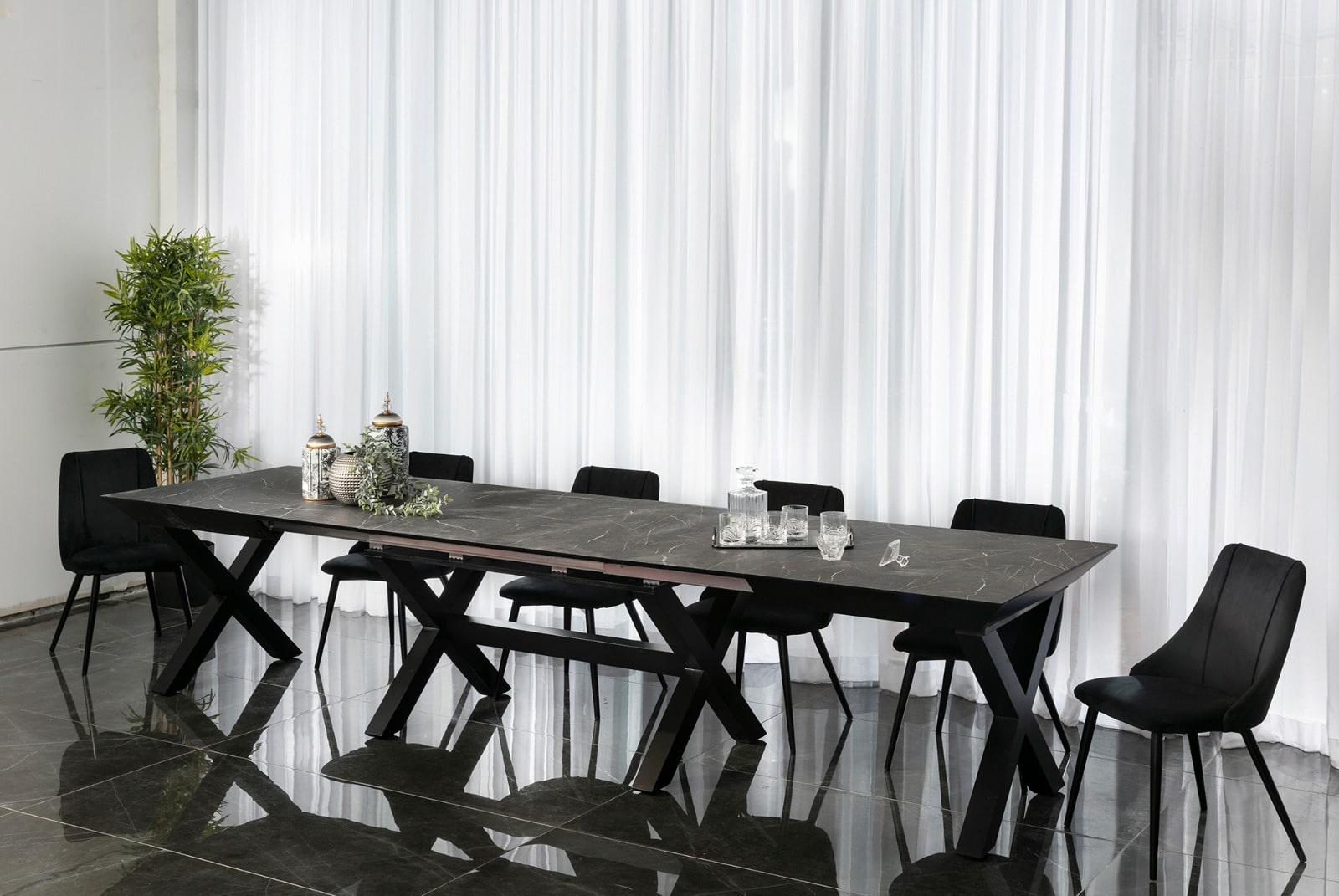 שולחן אוכל מודרני עם משטח כהה דמוי אבן ורגלי מתכת בעיצוב X.בשילוב כסאות מרופדים בצבע שחור בעיצוב עדין