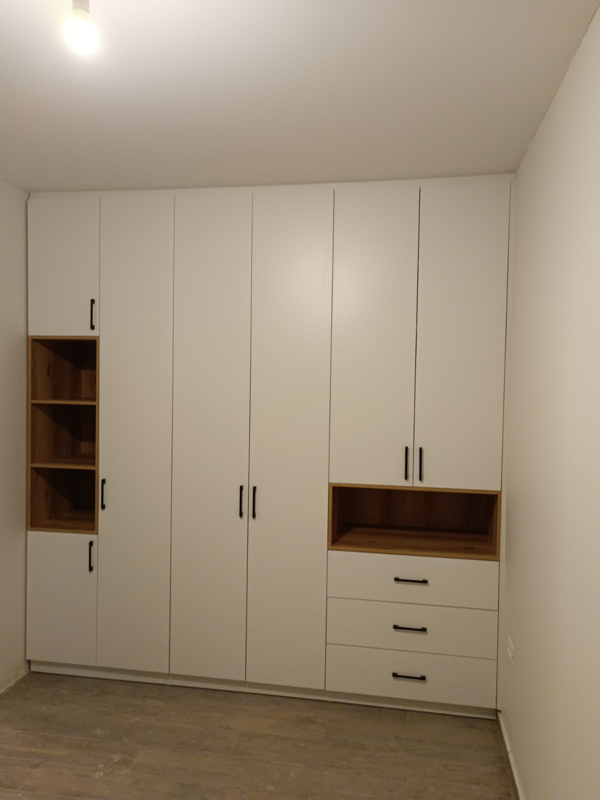 ארון בגדים עם חזית בהירה בקווים נקיים, משולב נישות פתוחות בגימור עץ, מגירות תחתונות וידיות כהות.