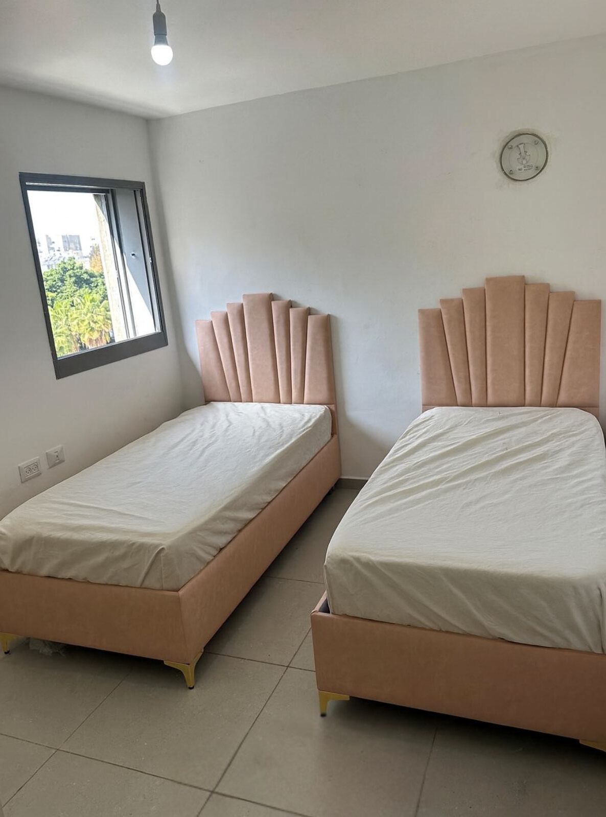 מיטות חדר שינה מרופדות בגוון ורוד בייבי עם ראשי מיטה מעוצבים בצורת מניפה ורגליים מוזהבות