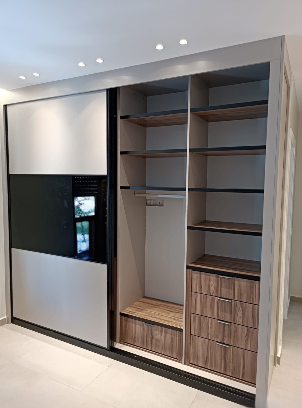 ארון הזזה בעיצוב מודרני עם חזית בקווים ישרים, שילוב גוונים בהירים וכהים ופרופיל דק, היוצרים מראה נקי ומאורגן. פנים הארון מתוכנן לניצול מקסימלי של החלל, עם מדפים, מגירות ואזור תלייה בגימור עץ בסטייל גבוה.