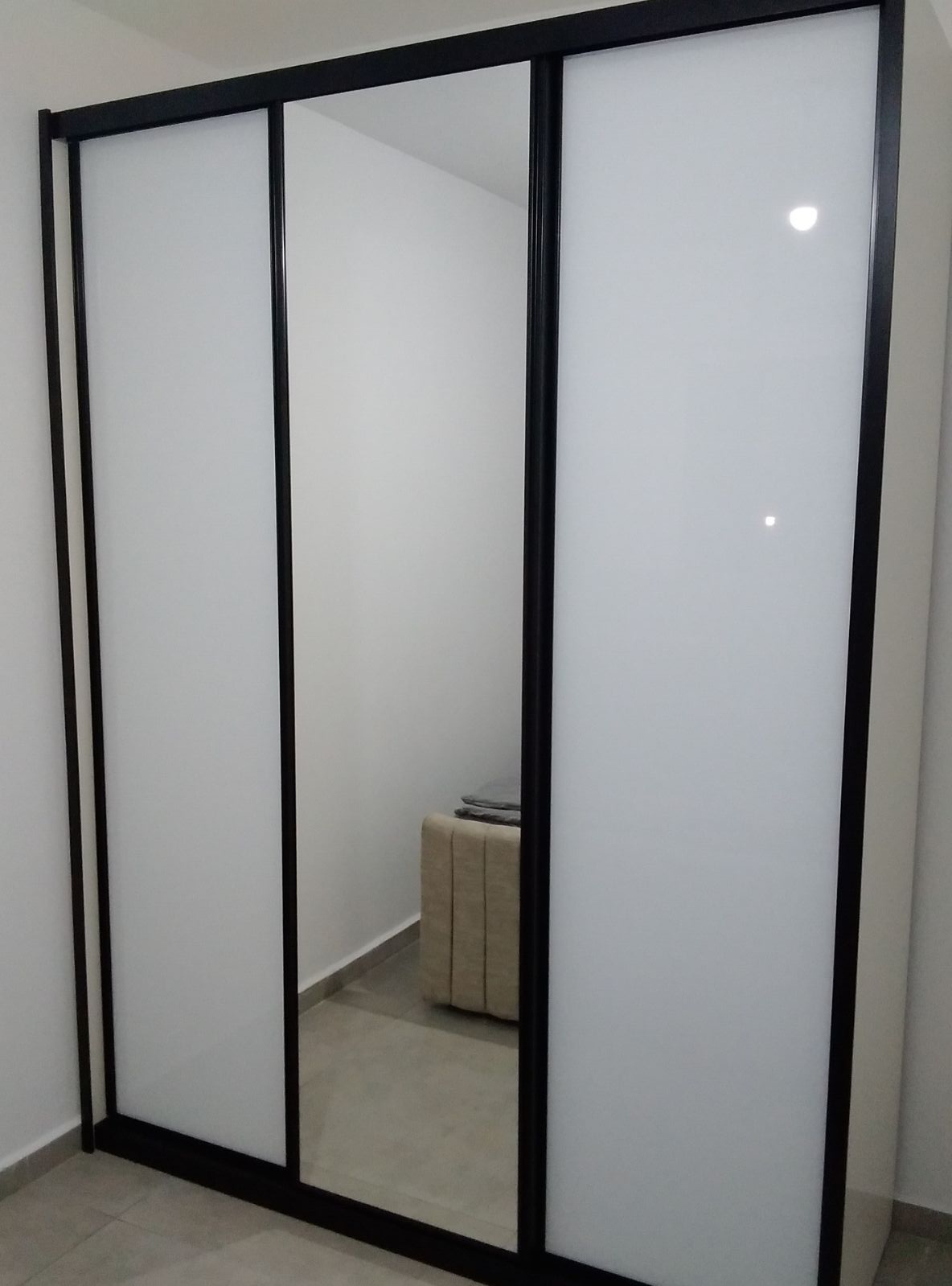 ארון הזזה מודרני עם דלתות זכוכית חלבית לבנה, למראה אלגנטי עם מראה מרכזית בשילוב מסגרת שחורה