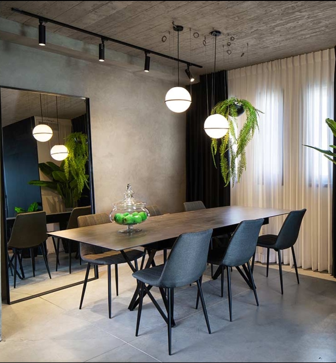 פינת אוכל מודרנית עם שולחן מלבני בעל משטח עץ טבעי ורגלי מתכת שחורות בעיצוב אלכסוני. הכיסאות המרופדים בגוון כהה.