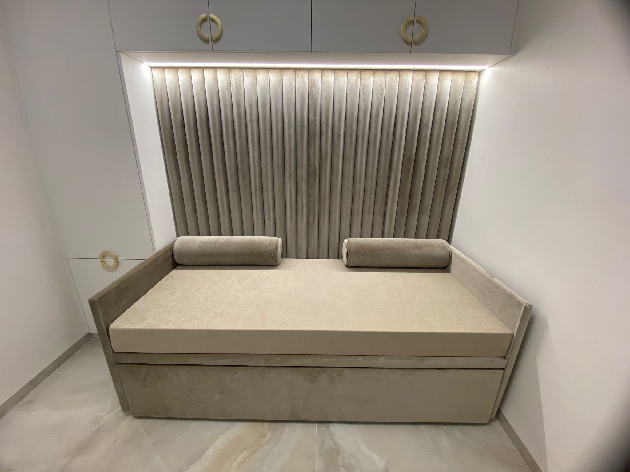 מיטת נוער מרופדת בעיצוב רך ואלגנטי, עם גב גבוה בעל קפלים אנכיים ותאורה נסתרת המוסיפה עומק ואווירה חמימה. הבסיס המרופד והכריות הגליליות משלימים מראה נעים.