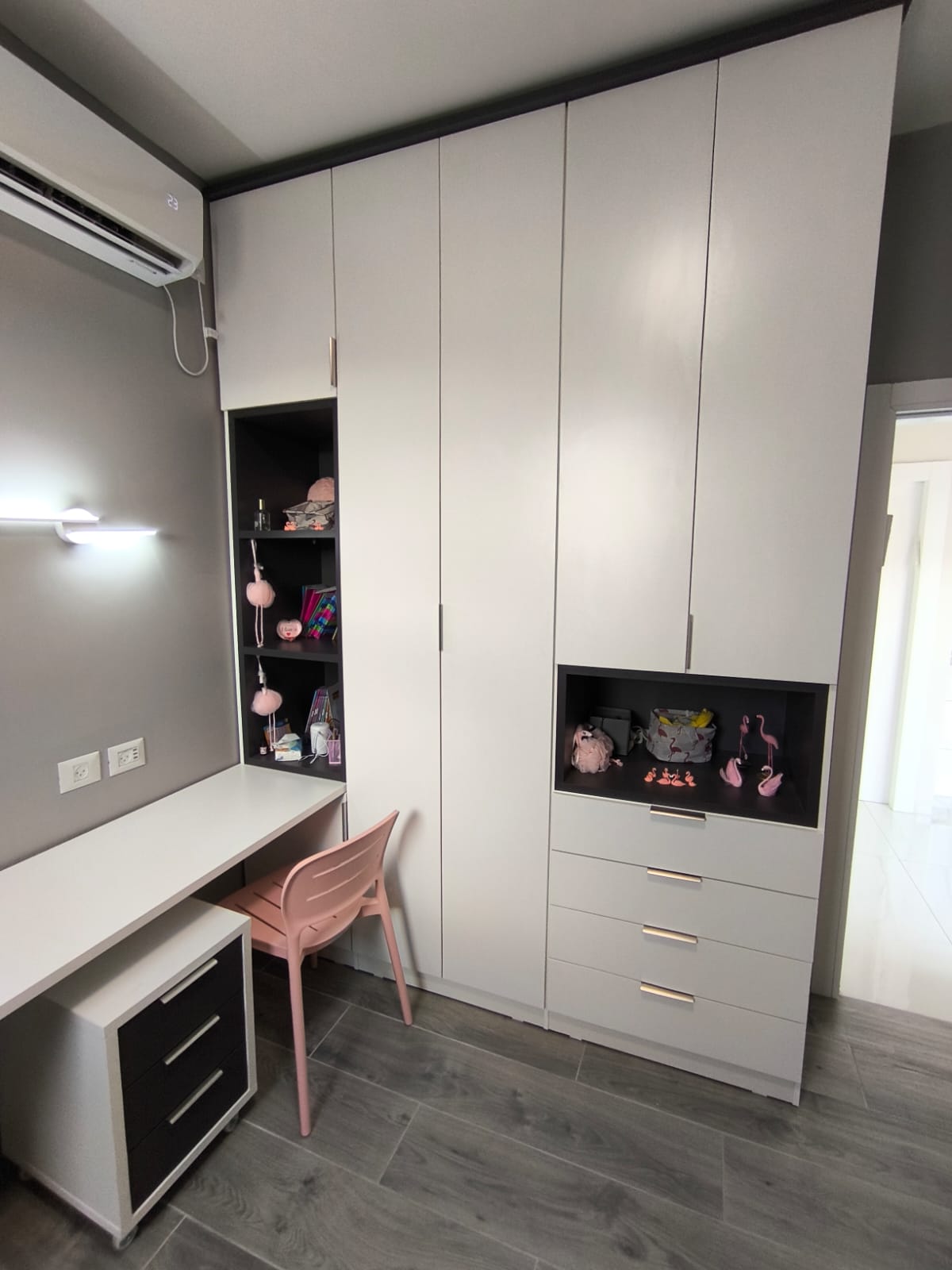 עם ארון בגדים בהיר בקווים נקיים, משולב עמדת עבודה רחבה ונישות פתוחות לאחסון ותצוגה.