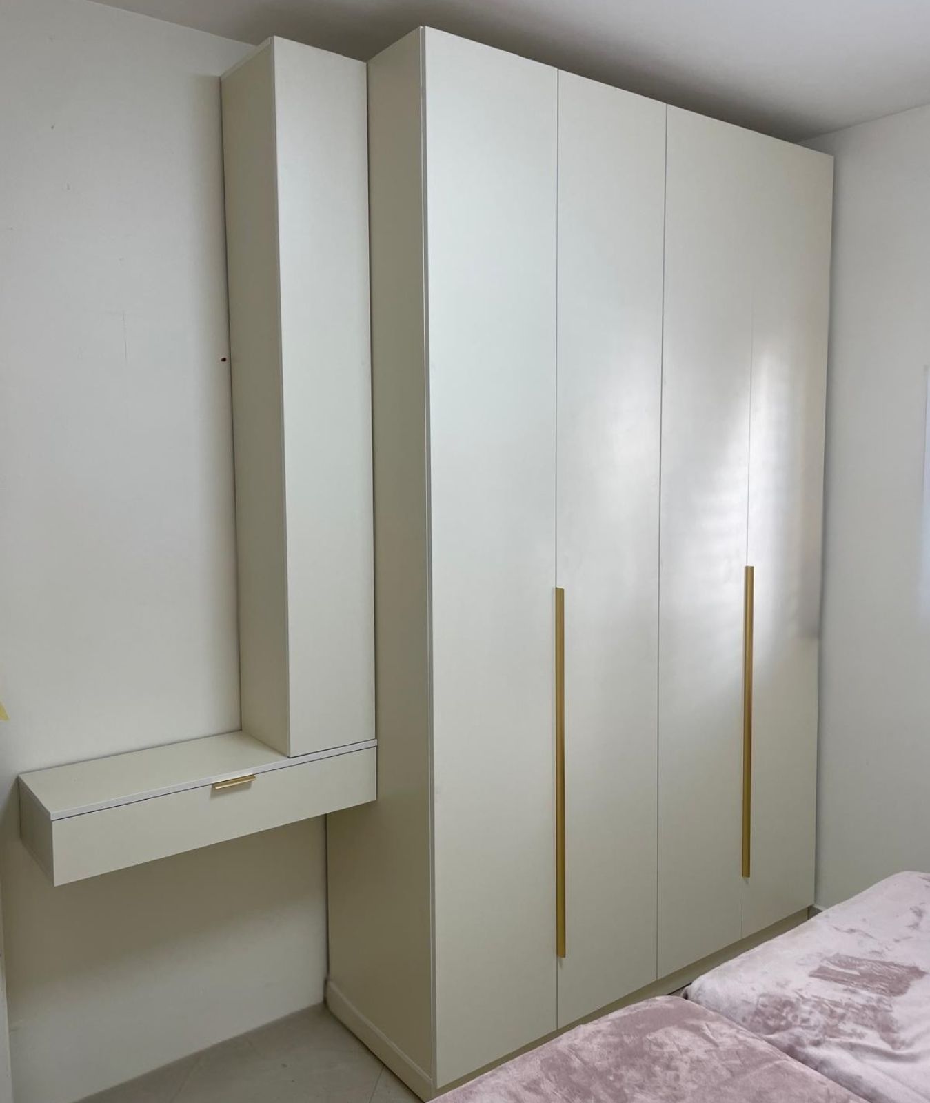 ארון בגדים גבוה ומעוצב בגוון שמנת נקי, המשלב ידיות זהב אנכיות וארוכות למראה יוקרתי. לצד הארון מותקנת יחידת נגרות משלימה הכוללת ארון אחסון צר וגבוה המחובר למגירה "מרחפת" רחבה. העיצוב המינימליסטי מנצל בצורה חכמה את גובה הקיר ויוצר פתרון אחסון פונקציונלי והרמוני בחלל החדר.