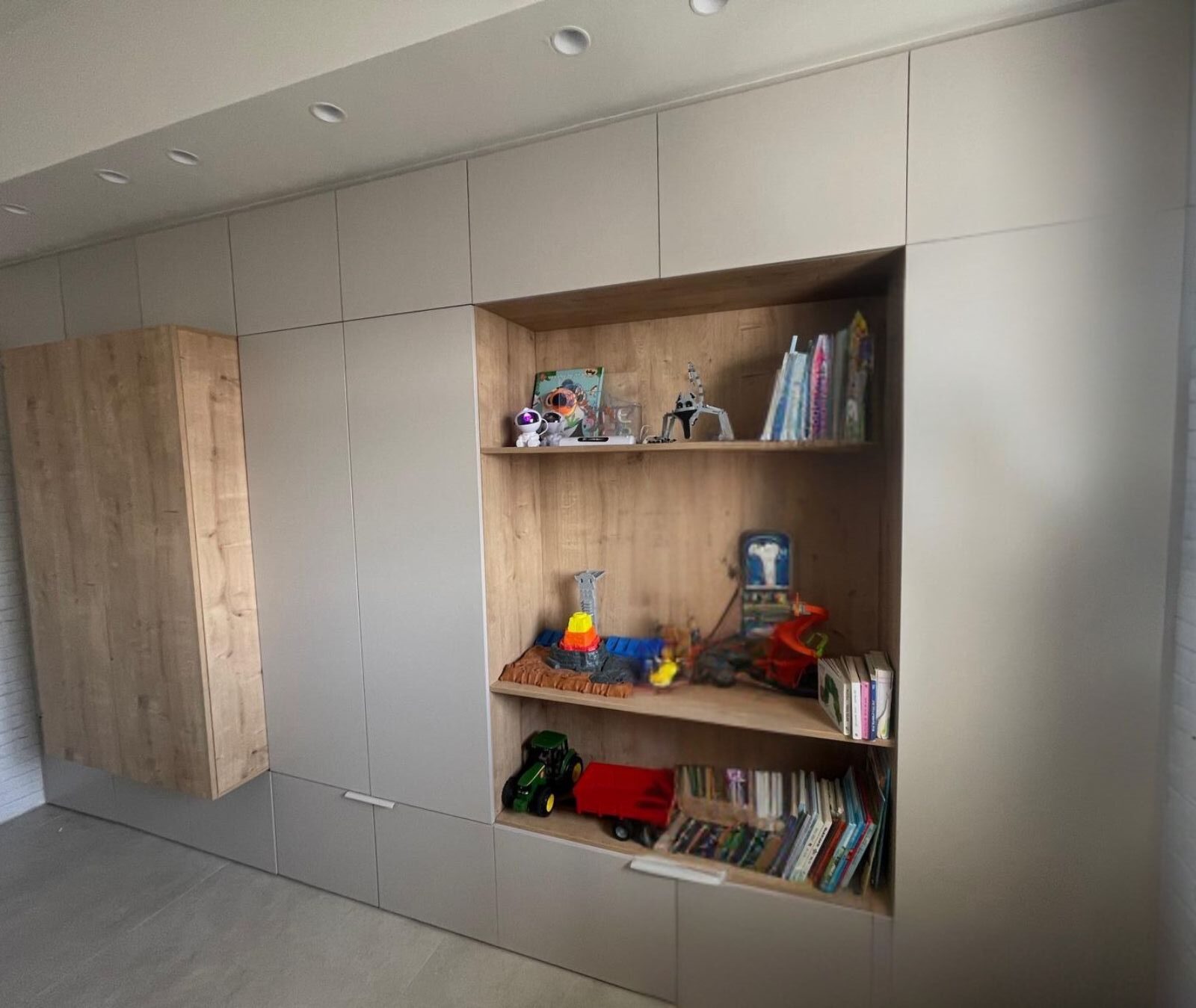 ארון קיר רחב ומעוצב לחדר ילדים, המנצל את כל שטח הקיר לאחסון ותצוגה. הארון משלב חזיתות בהירות בגוון סהרה עם פתיחת "טאץ'" נקייה, לצד נישת מדפים פתוחה מעץ בגוון טבעי וחמים. בצד שמאל משולבת יחידת ארון מובלטת "מרחפת" תואמת מעץ, היוצרת מראה מודרני, מאורגן ופונקציונלי מאוד.