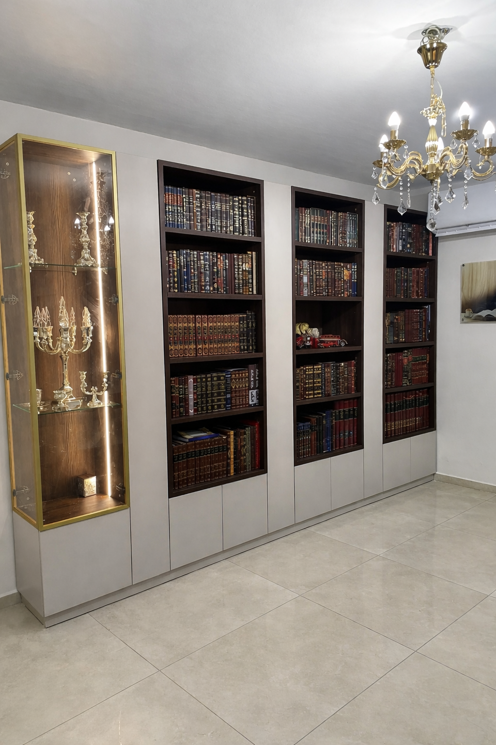 ספריית קודש יוקרתית המשלבת בין תצוגה מעוצבת לאחסון פרקטי. המבנה כולל שלוש יחידות מדפים פתוחות מעץ כהה עם פסי הפרדה מוזהבים, לצד ויטרינת זכוכית מוארת עם מסגרת זהב. כל חלקי הספרייה מוקפים בארונות אחסון סגורים בגימור בהיר וחלק (החלק התחתון והמחיצות), המעניקים מראה נקי ומודרני יחד עם ניצול מקסימלי של שטח הקיר לאחסון נסתר.